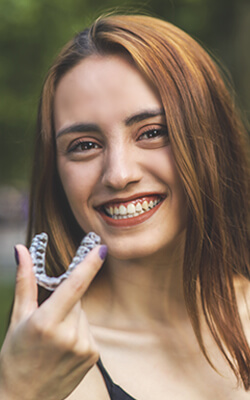 Woman smiling while holding up her Invisalign aligner