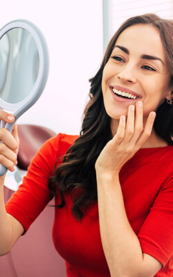 Woman looking at her smile in a handheld mirror after dental treatment