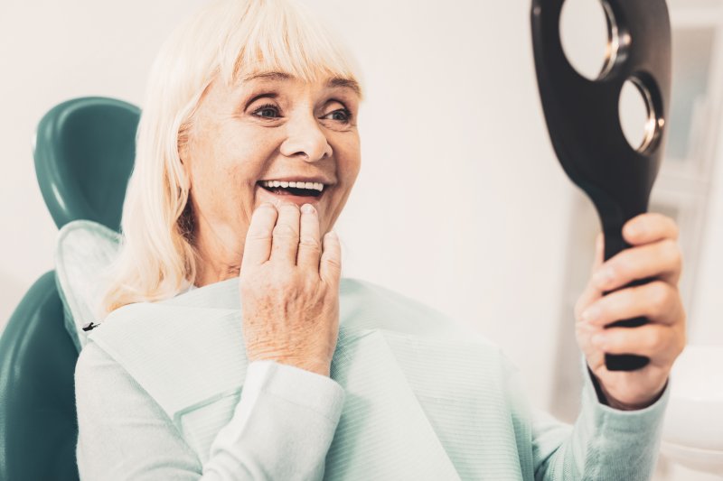 An older woman looking at her dentures with a hand mirror