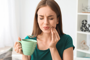 Woman with cup of coffee rubbing jaw due to dental implant sensitivity