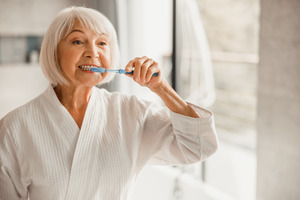 Senior woman in bathrobe brushing her teeth